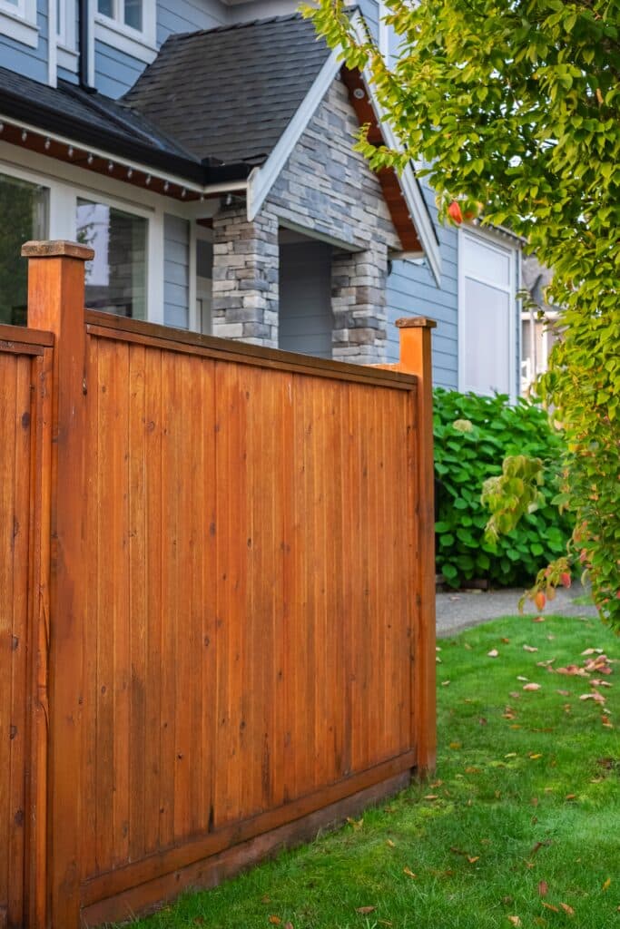 Picture of a wood fence with a house in the background. green grass and trees 